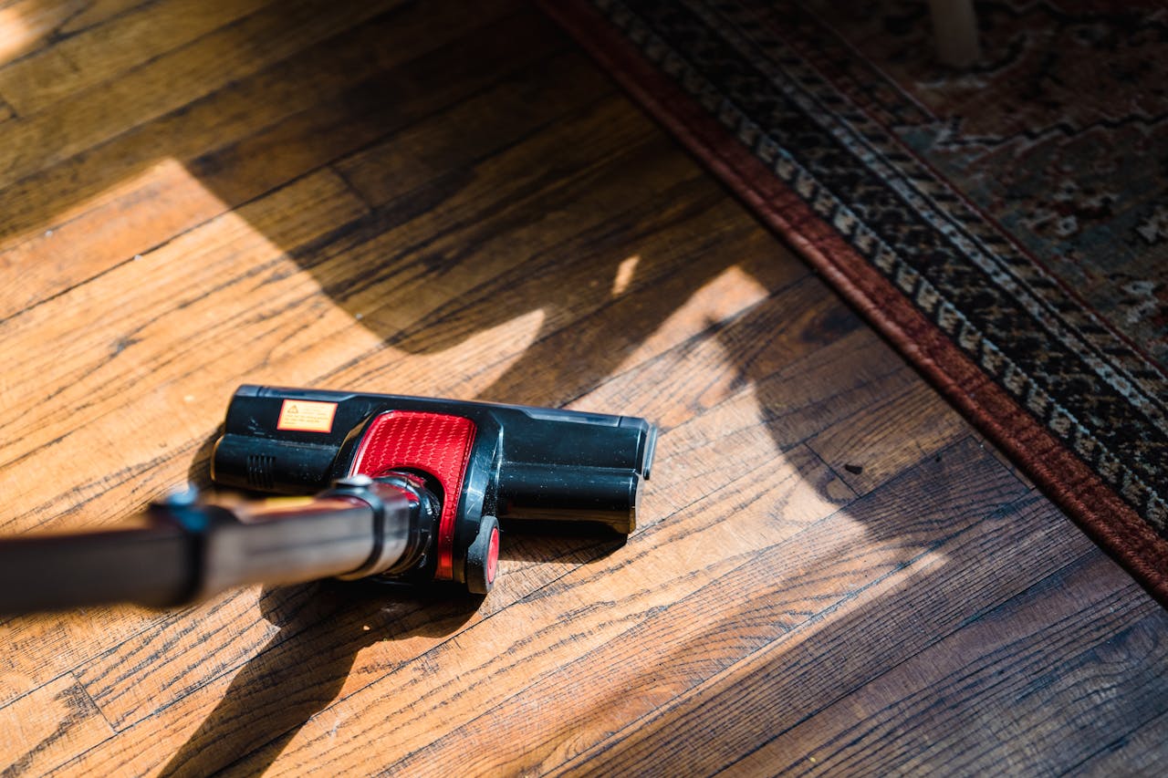 hero-img-01 Close-up of a vacuum cleaner on wooden flooring near a patterned rug, showcasing domestic cleaning.